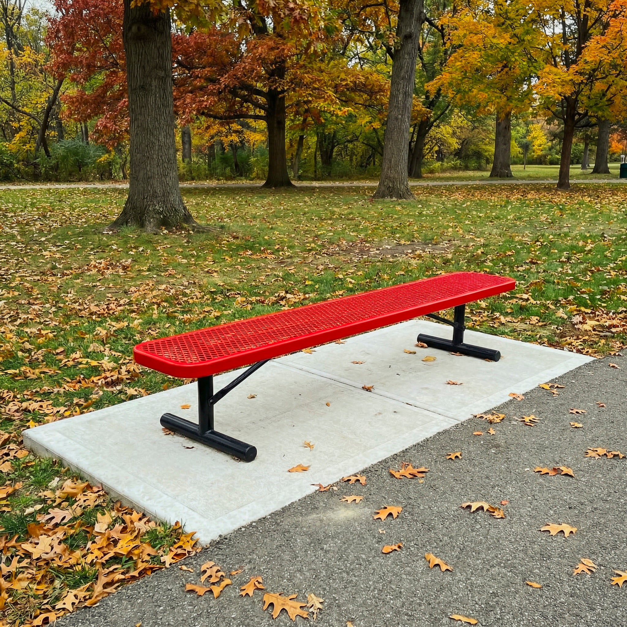 Red metal bench in a park with autumn leaves and trees in the background