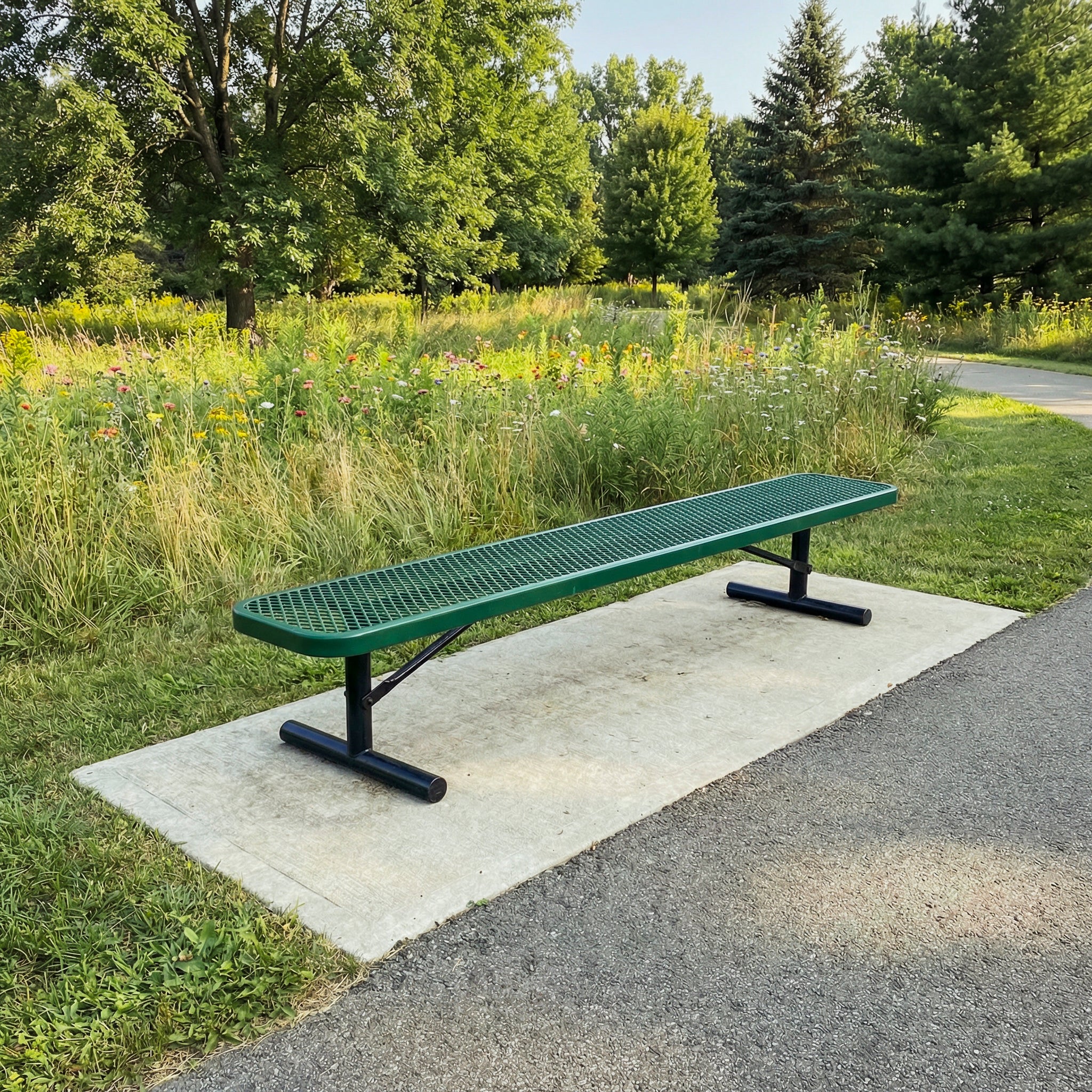 Green metal bench on a concrete slab in a park setting with trees and grass.