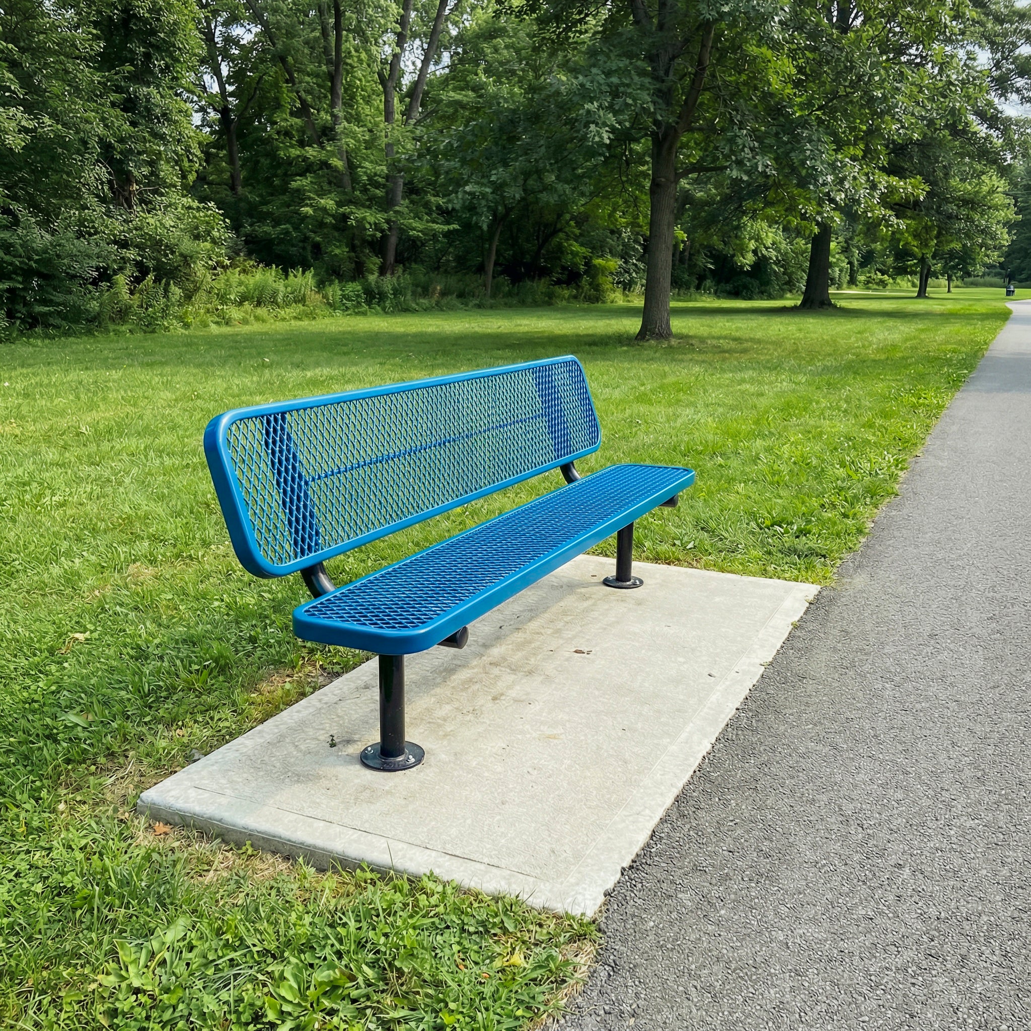 Blue metal bench on a concrete platform in a park with green grass and trees.
