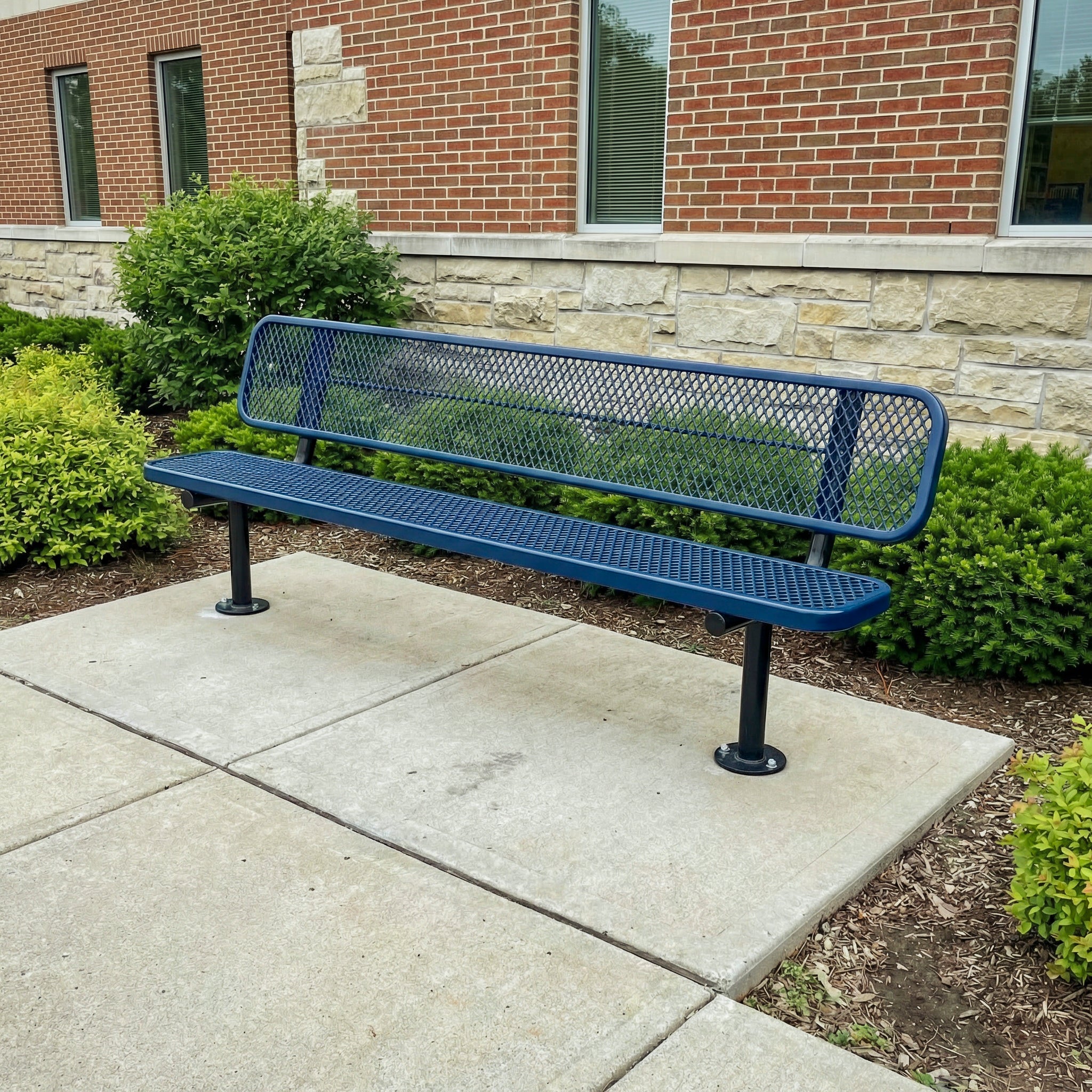 Blue metal bench on a concrete patio in front of a brick building.
