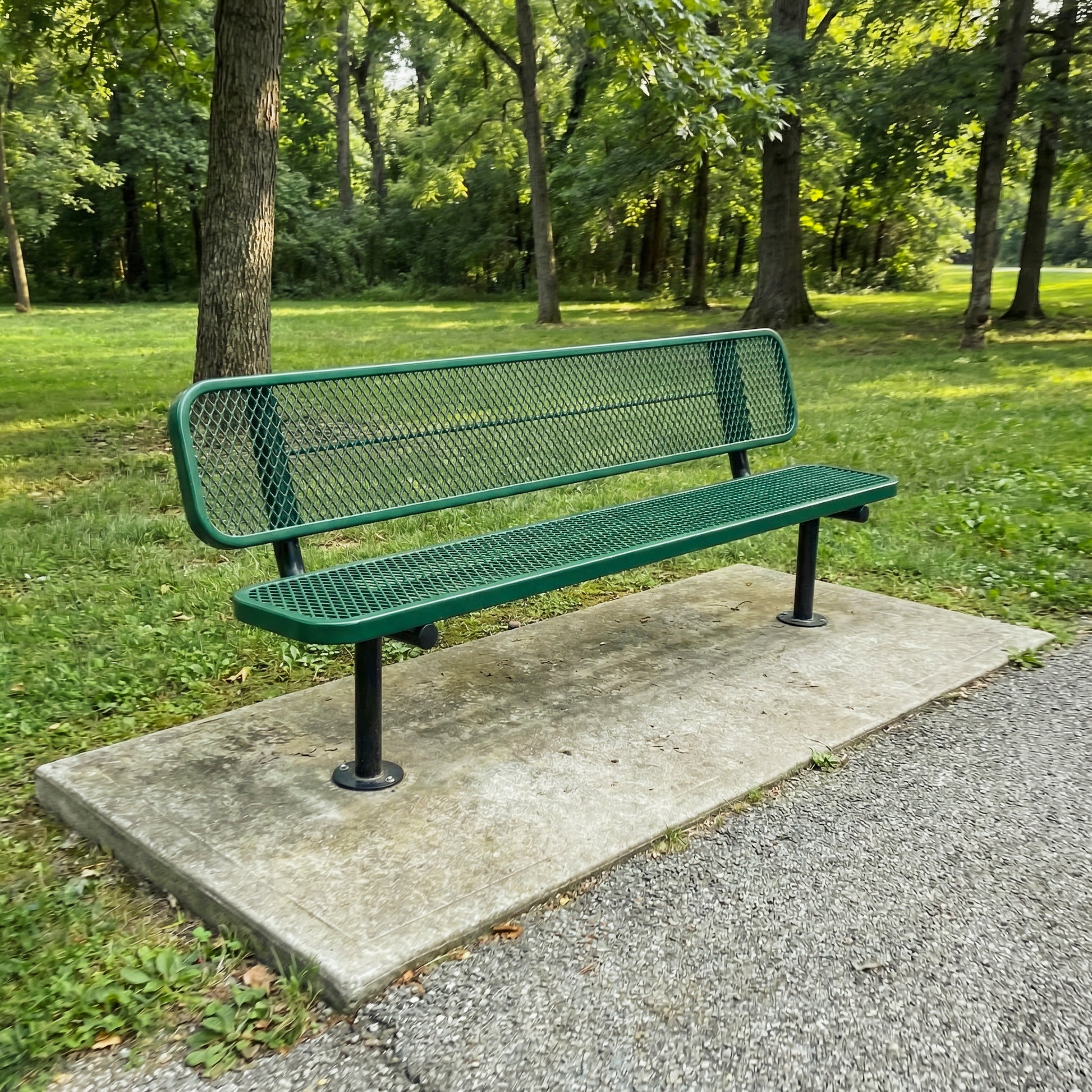 Green metal bench on a concrete platform in a park with trees in the background