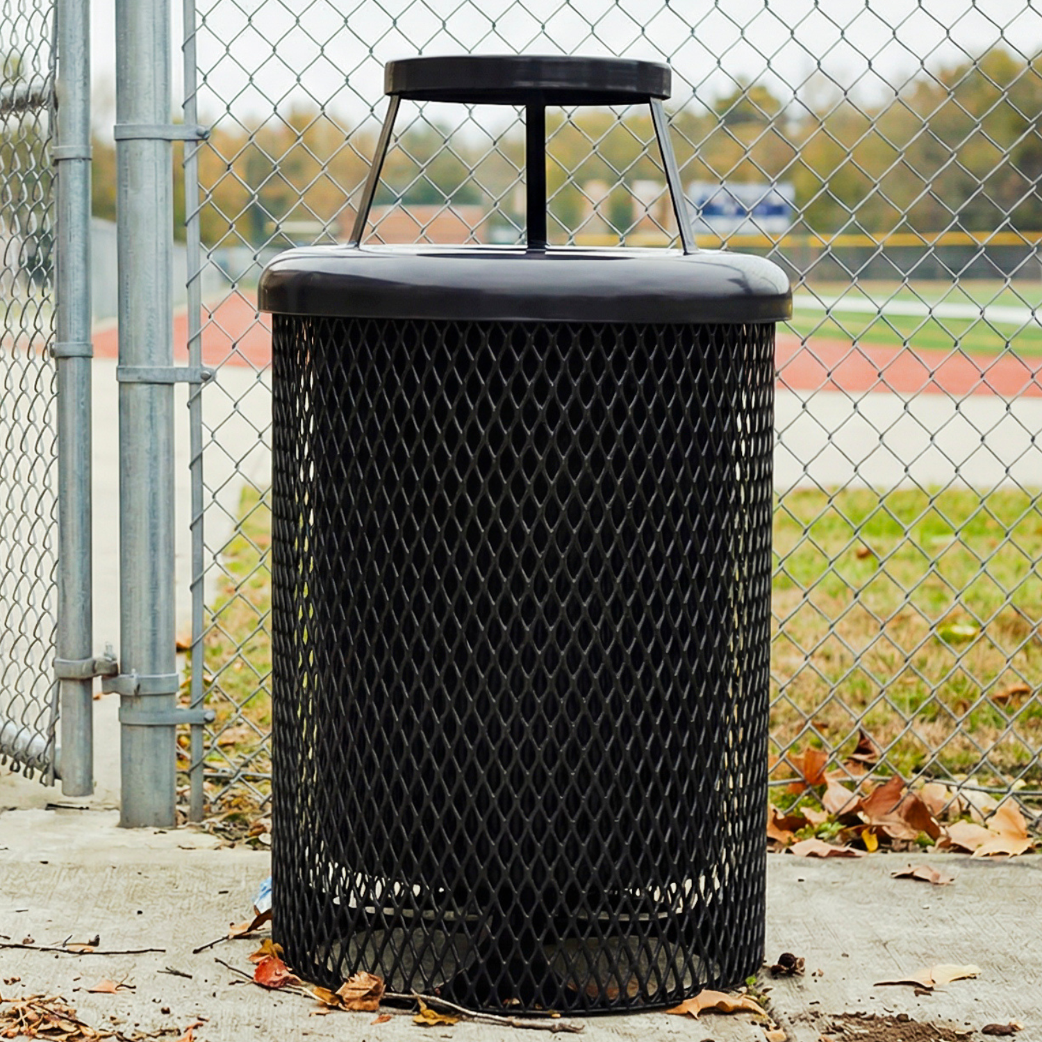 Black metal trash can with a chain-link fence and outdoor setting in the background
