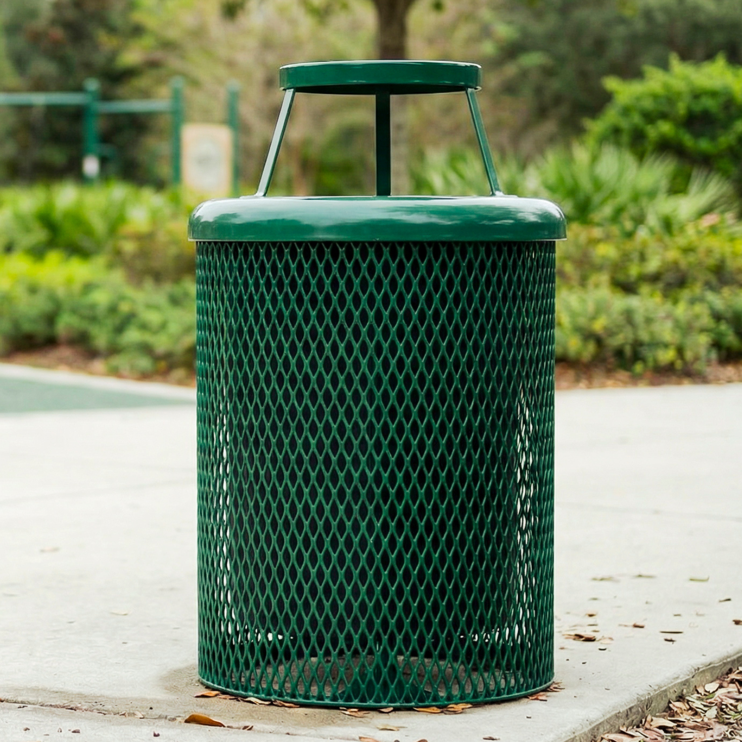 Green metal trash can with textured surface on a pathway