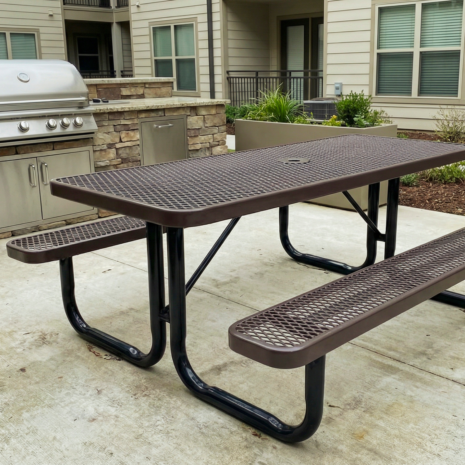 Brown metal picnic table on a patio with a grill and building in the background