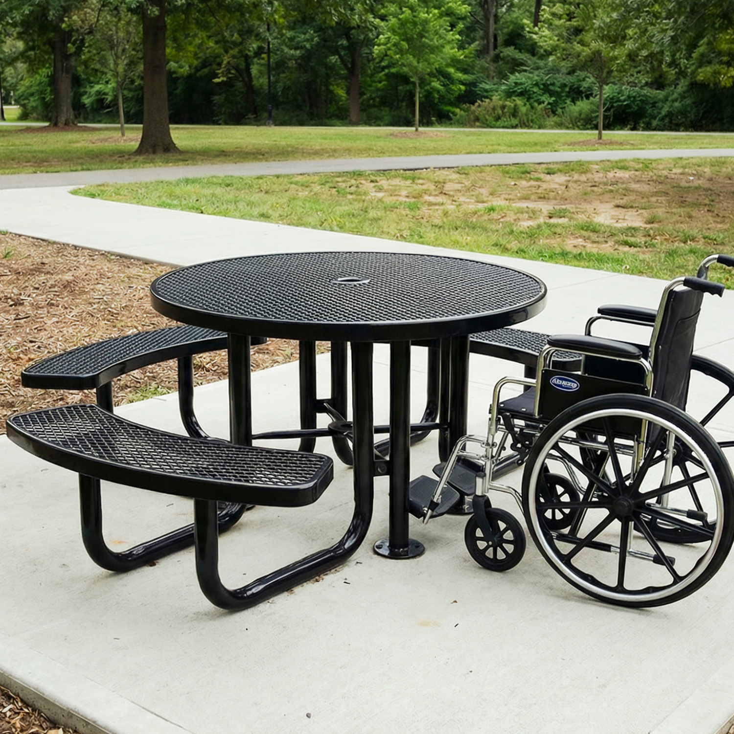 Black metal picnic table with wheelchair on a paved path in a park.