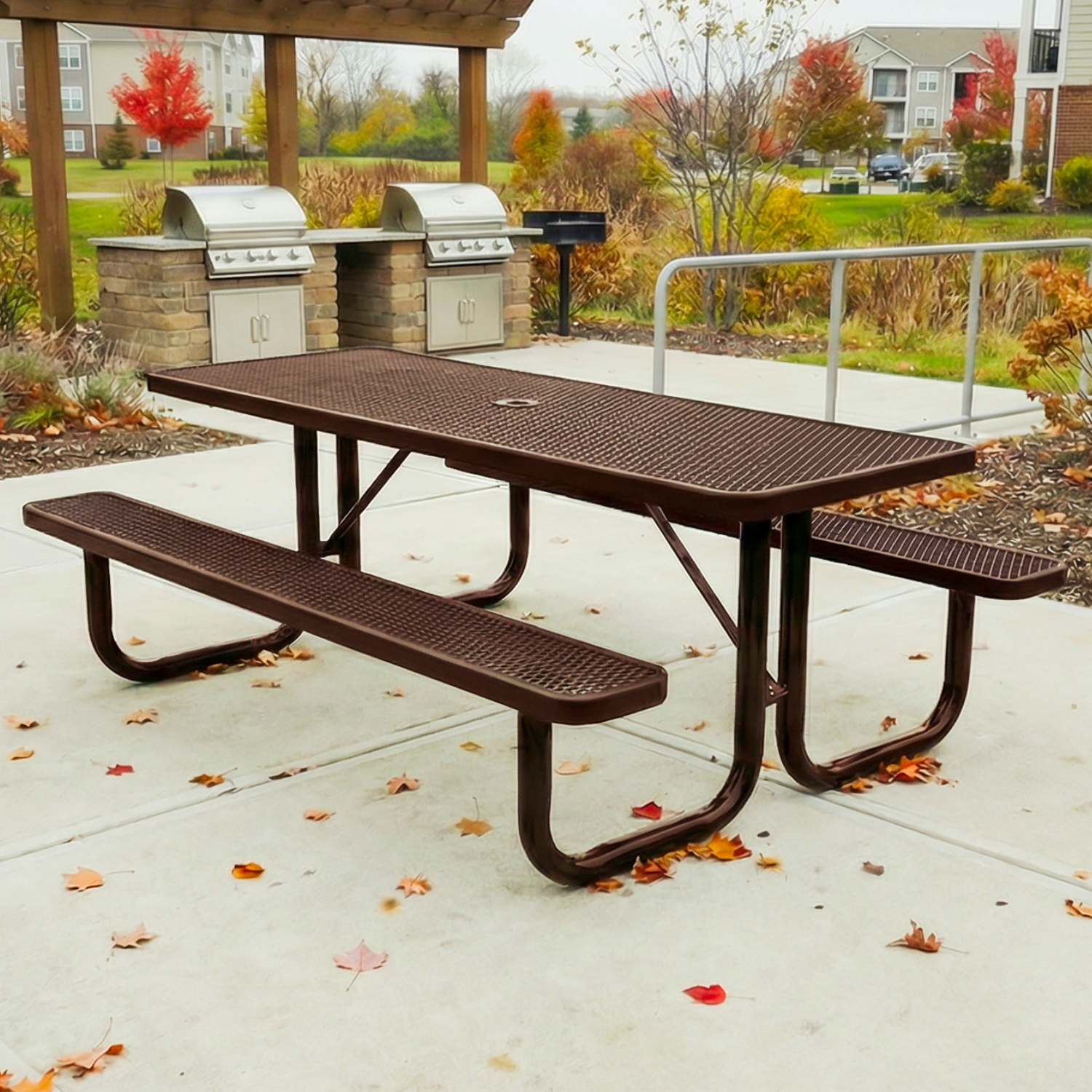 Metal picnic table with benches on a concrete surface, surrounded by autumn leaves.