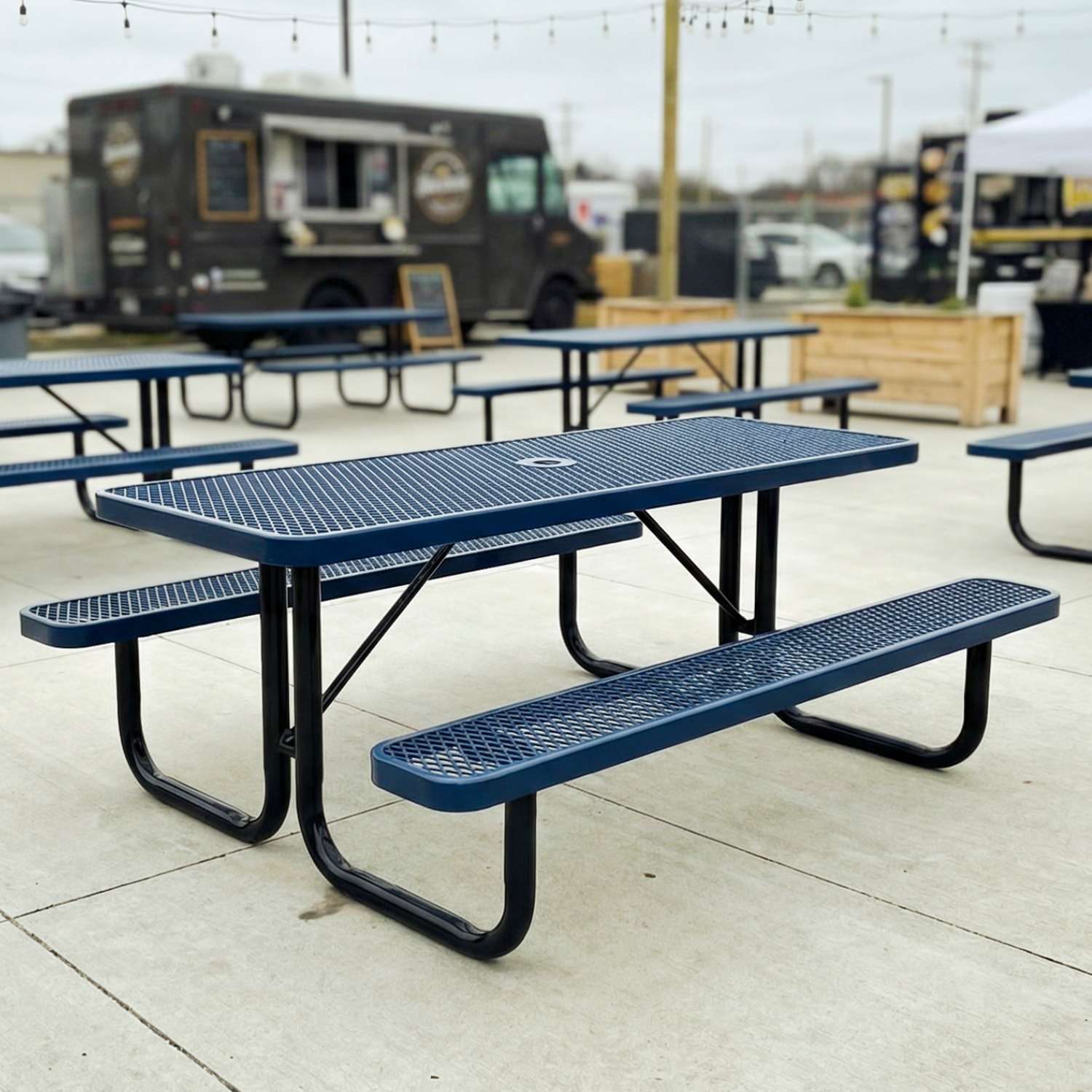 Blue picnic tables in an outdoor setting with food trucks in the background