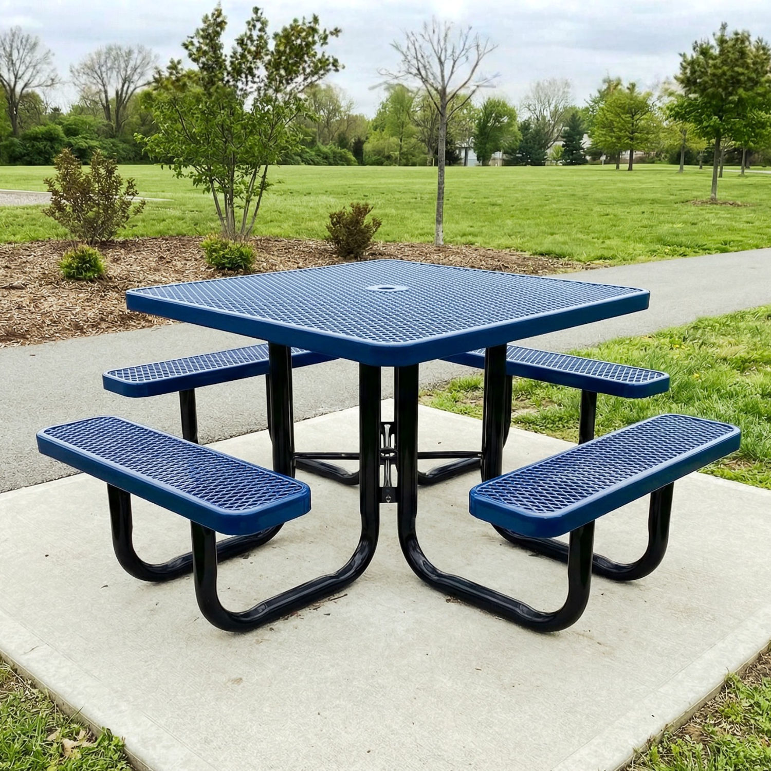 Dark blue square picnic table with four benches on a concrete pad in a park setting.