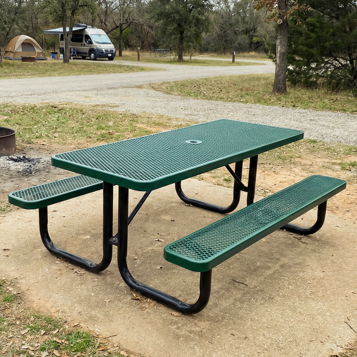 Green picnic table with benches in a park setting with trees and a camper in the background.