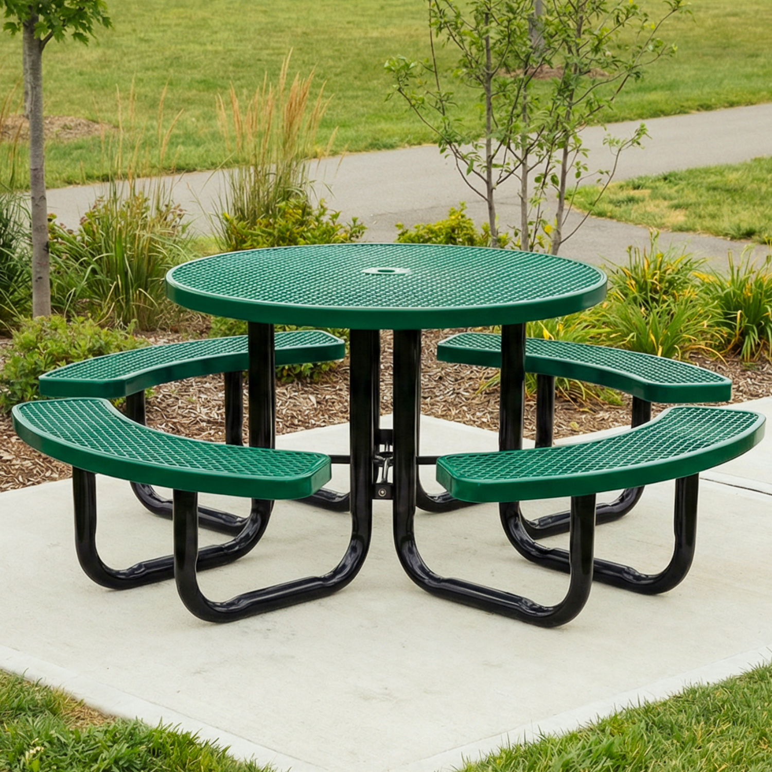 Green metal picnic table with four curved benches on a concrete slab in a park setting.