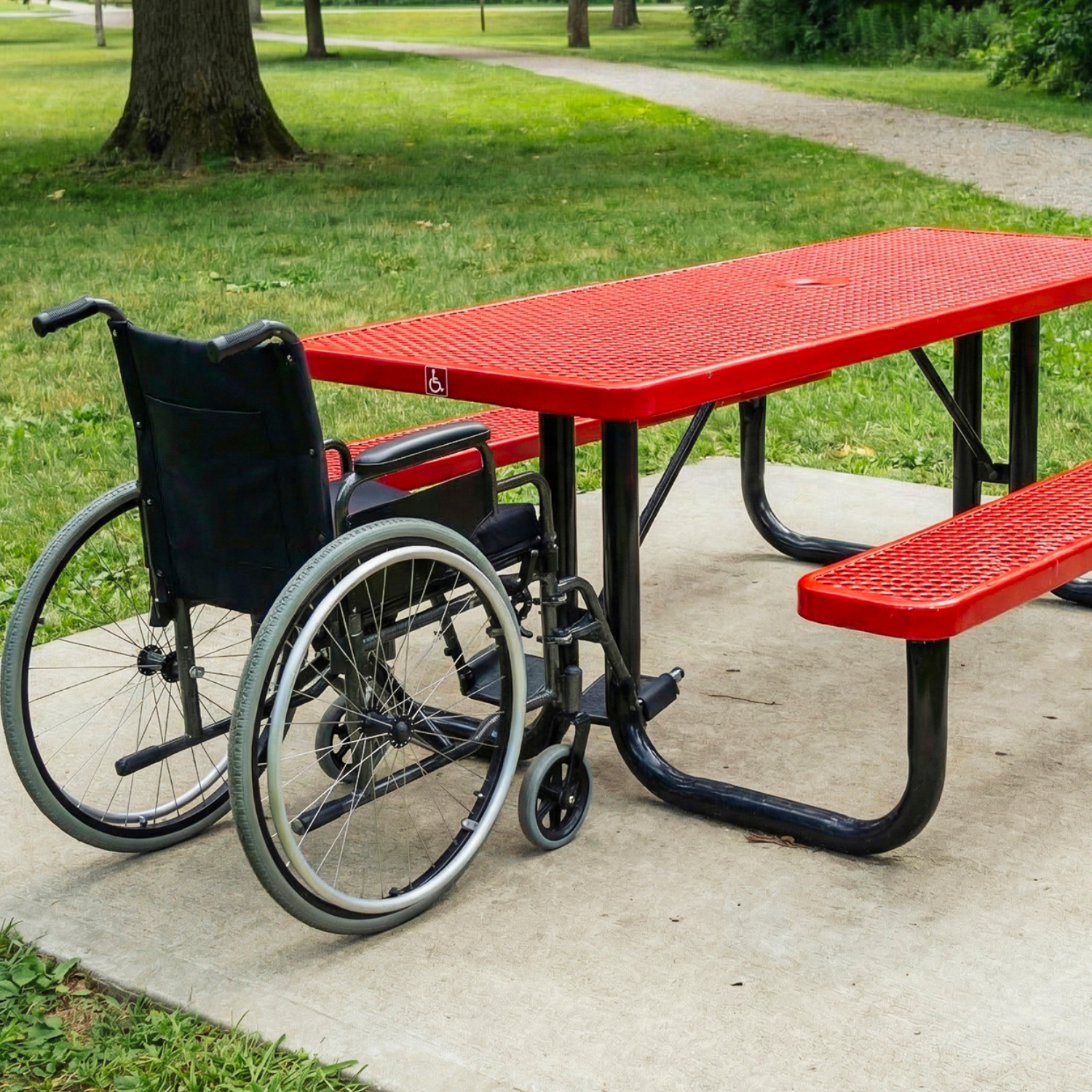 Red ADA picnic table with a wheelchair next to it on a sidewalk in a park.