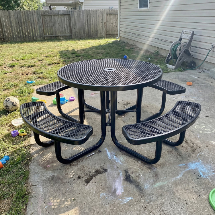 Black metal picnic table with benches on a concrete patio, surrounded by toys and a grassy area.