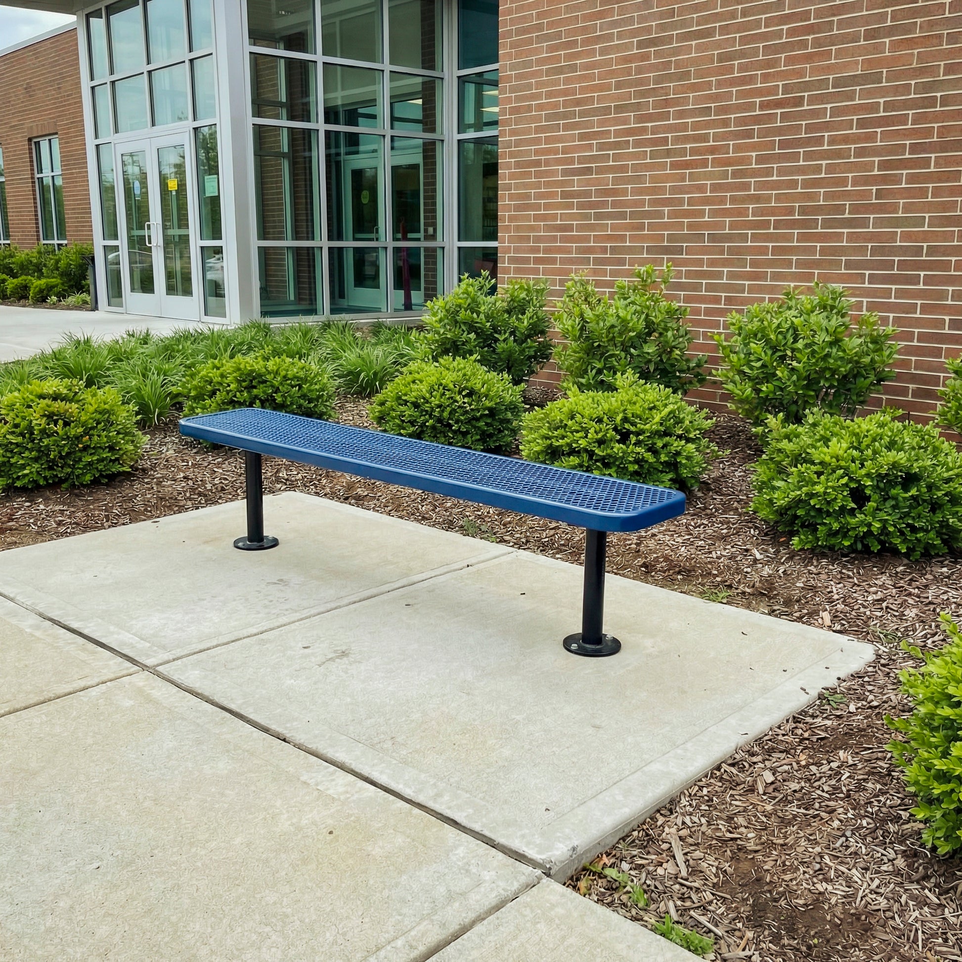 Blue bench on a concrete patio in front of a brick building with greenery.