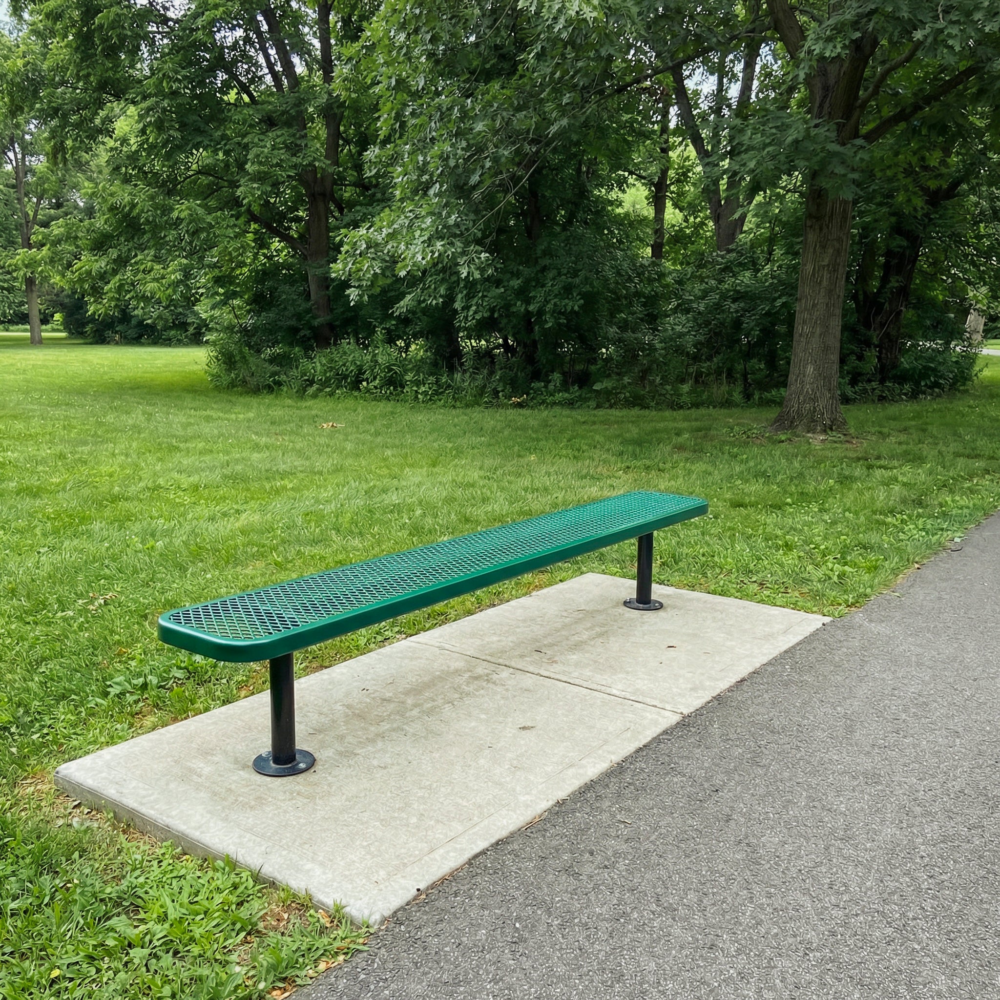 Green bench on a concrete slab in a park with grass and trees in the background