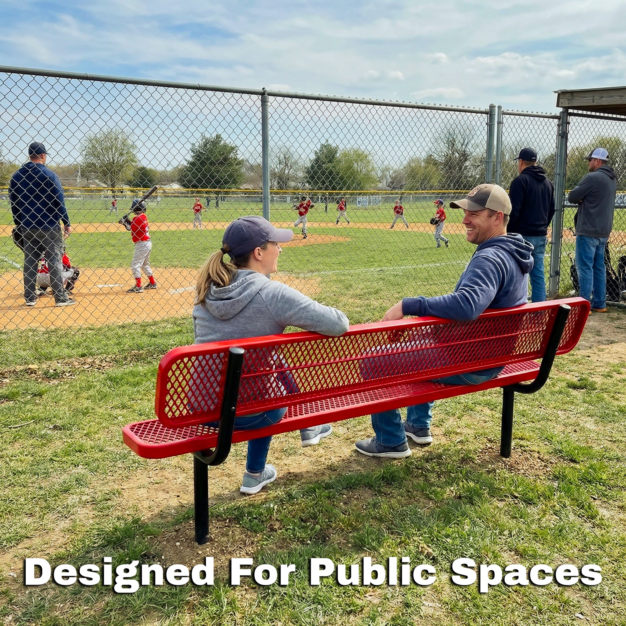 Two people sitting on a red bench at a baseball field with 'Designed For Public Spaces' text.
