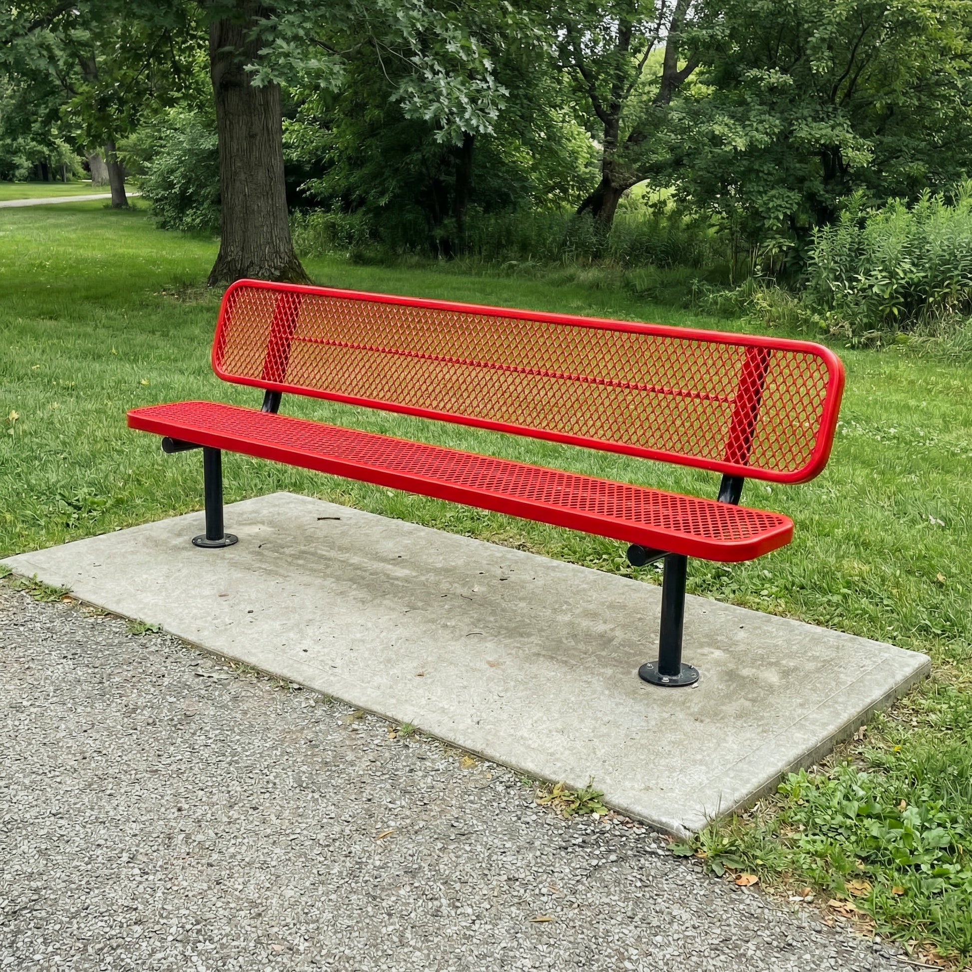 Red metal bench on a concrete platform in a park setting with green grass and trees.